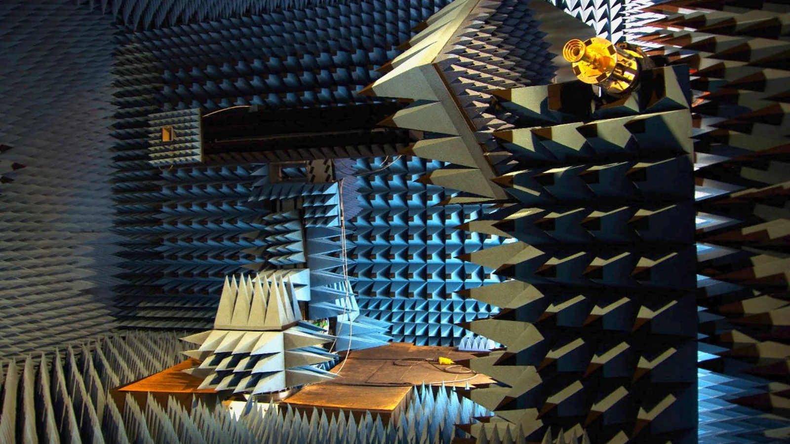 Radio frequency anechoic chamber lined with blue absorber cones, with a positioning mast and a test antenna